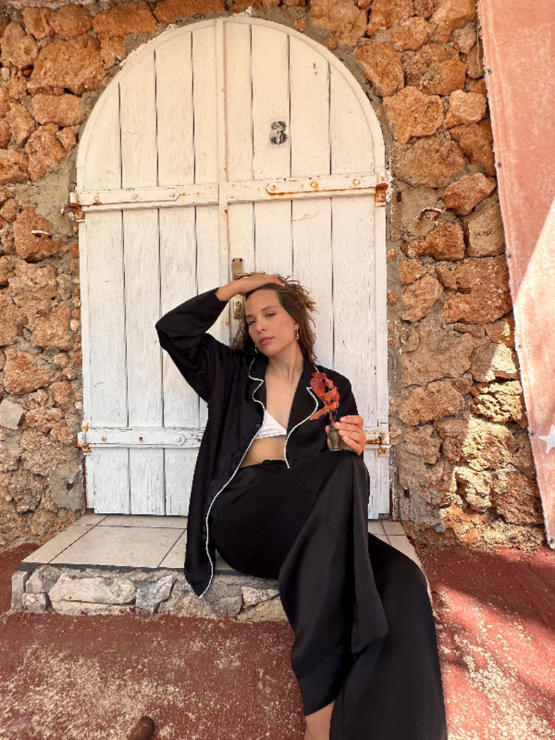 Woman sitting in front of a white door on a stone wall wearing Shivani Pure Silk pajama set