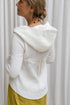 A woman wearing a white hoodie with a zipper and a flowing hood, paired with yellow pants. Back view