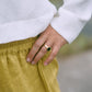 A woman wearing a white hoodie with a zipper and a flowing hood, paired with yellow pants. Detail view.