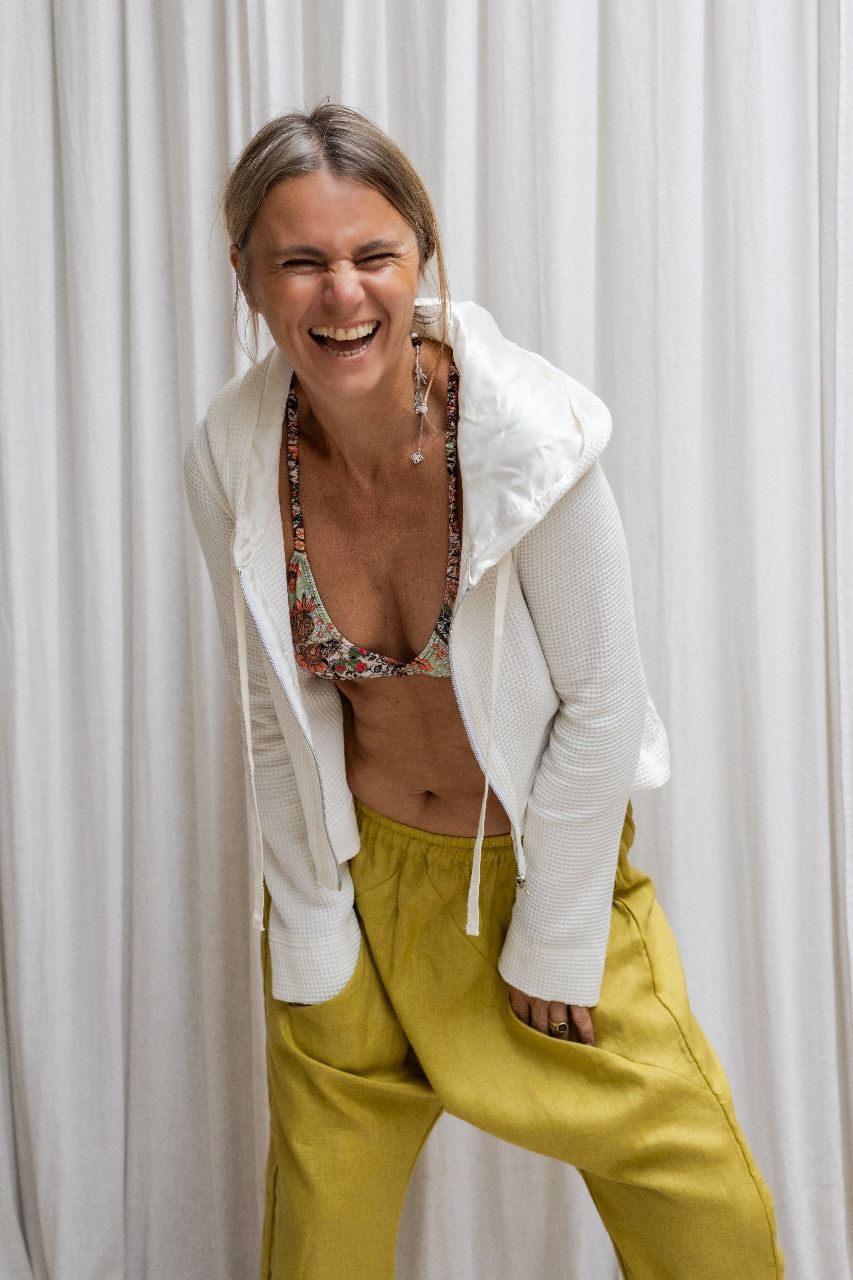 A woman wearing a white hoodie with a zipper and a flowing hood, paired with yellow pants. and viscose flowery bra