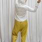 A woman wearing a white hoodie with a zipper and a flowing hood, paired with yellow pants. Back view.