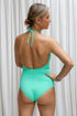 A woman, posing in front of a white backfround, is wearing the Vipasha One-Piece Swimwear, in a striking shade of emerald, back view.