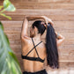 Woman in black silk bra and silk black pajamas standing against a wooden wall.