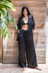 Woman wearing a black ssilk pajamas standing against a wooden wall.