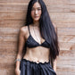 Woman wearing a black ssilk pajama bottom with silk bra  standing against a wooden wall.