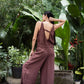 Woman in a brown linen jumpsuit standing in a lush, green garden.