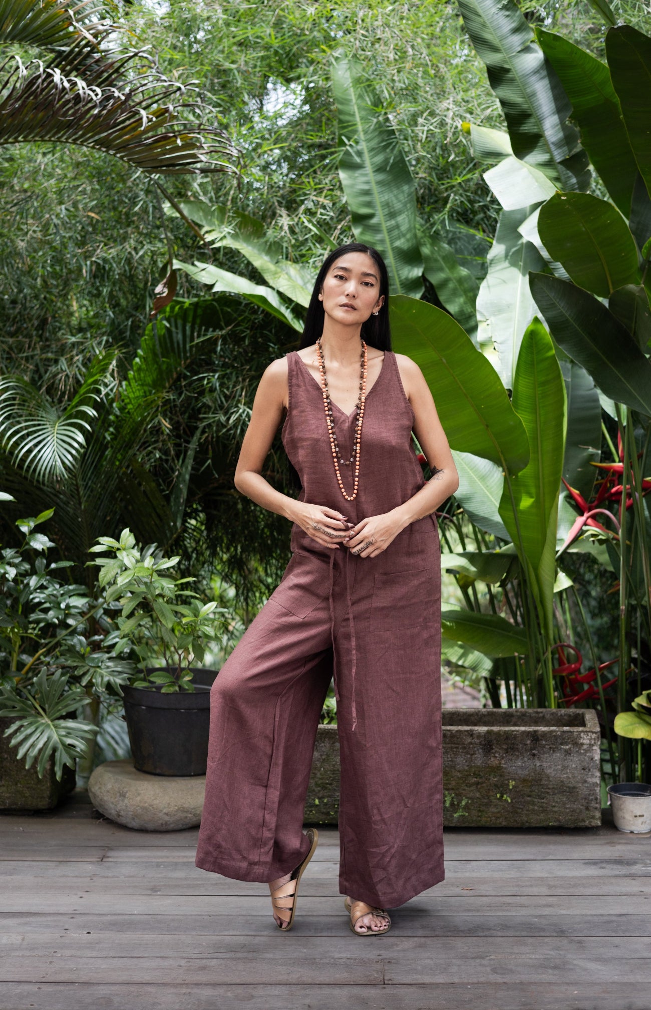 Woman in a brown linen jumpsuit standing in a lush garden