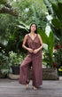Woman in a brown linen jumpsuit standing in a lush garden