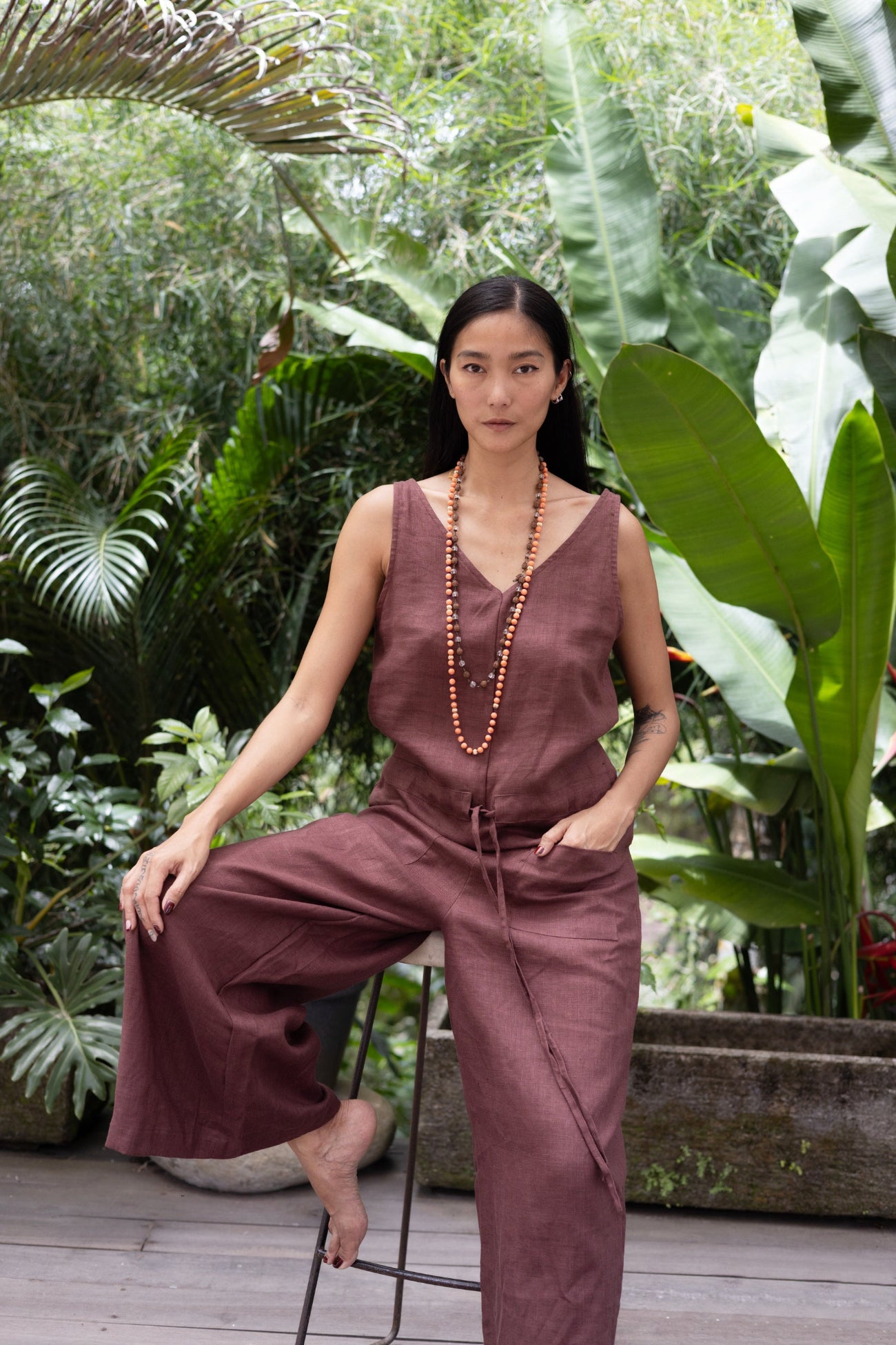 Woman in a linen jumpsuit sitting among tropical plants