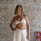 A woman wearing a white 100% cotton bra and linen pants, standing against a textured background.