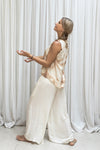 A woman standing in a relaxed pose wearing a tea-dyed, sleeveless, silk top paired with matching pants.